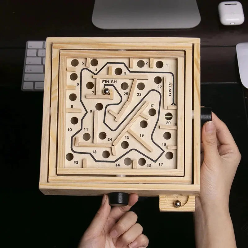 Wooden maze game held by a hand with a computer keyboard in the background