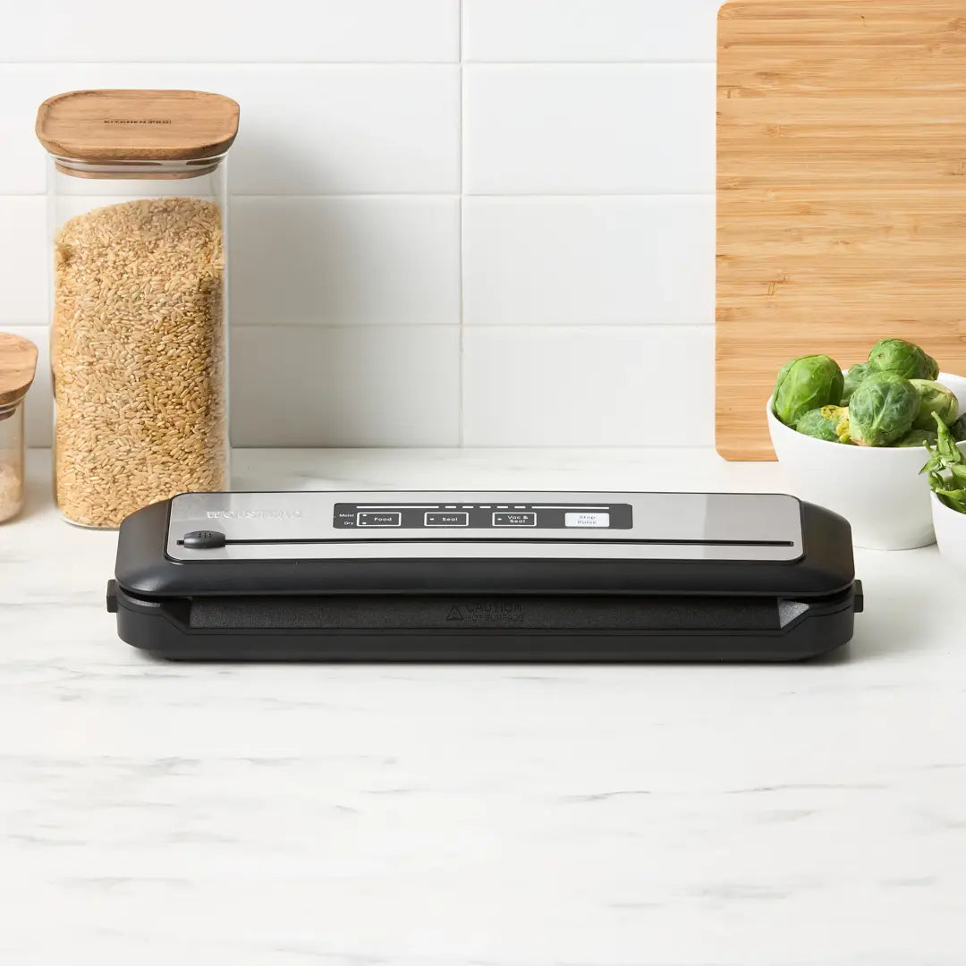 Black food vacuum sealer on a kitchen counter with jars and vegetables in the background