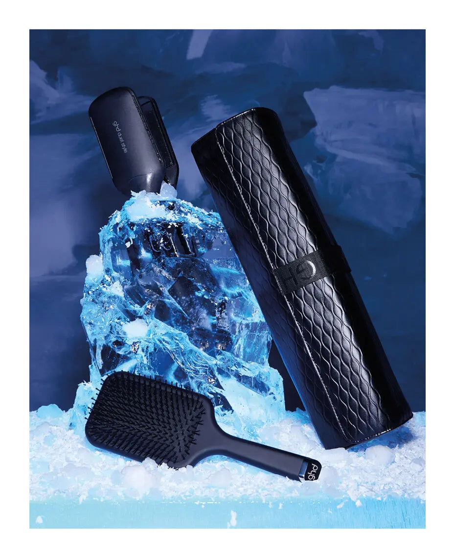 Black hair care products including a hair dryer, brush, and case on a blue textured background