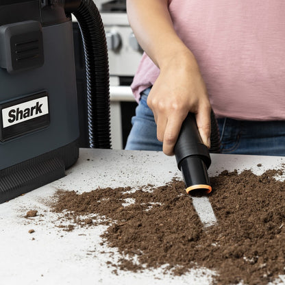 Person using a Shark vacuum cleaner on a surface with dirt and debris.