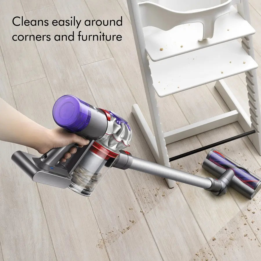 Hand holding a purple and gray vacuum cleaner on a wooden floor with text 'Cleans easily around corners and furniture'.
