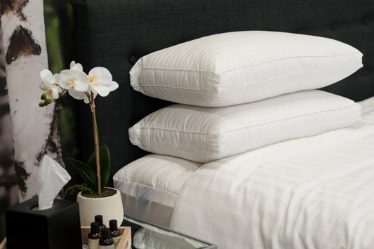 Stack of white pillows on a bed with a flower arrangement and small table in the foreground.