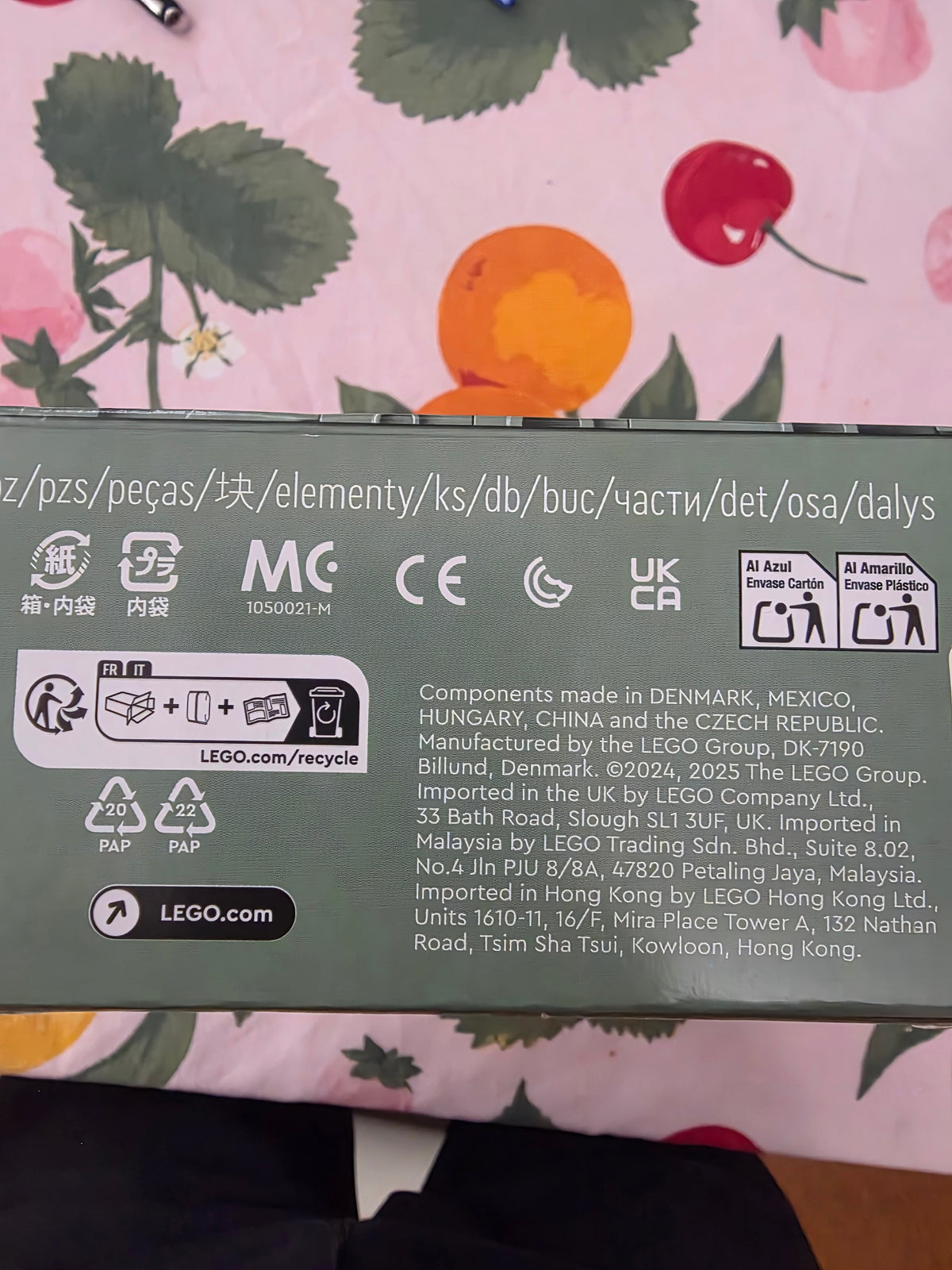 The back of a LEGO toy box with product information, logos, and component text, photographed over a pink patterned fabric background.