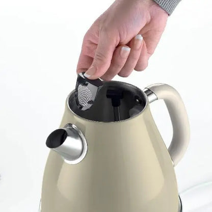 Beige kettle with a hand placing a black tea infuser into it on a white background