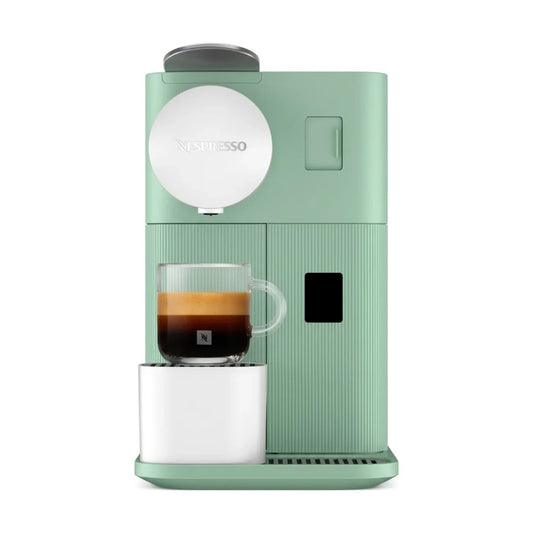 Nespresso coffee machine in a muted sage green color, shown with a glass cup of espresso on the drip tray against a plain white background.