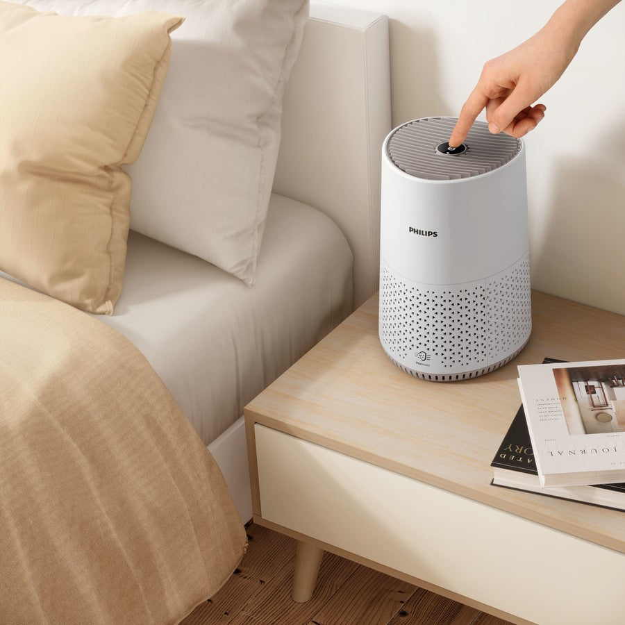 Philips air purifier on a wooden side table with a hand touching it, in a living room setting.