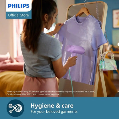 Woman using a Philips garment steamer on a shirt in a bedroom setting.