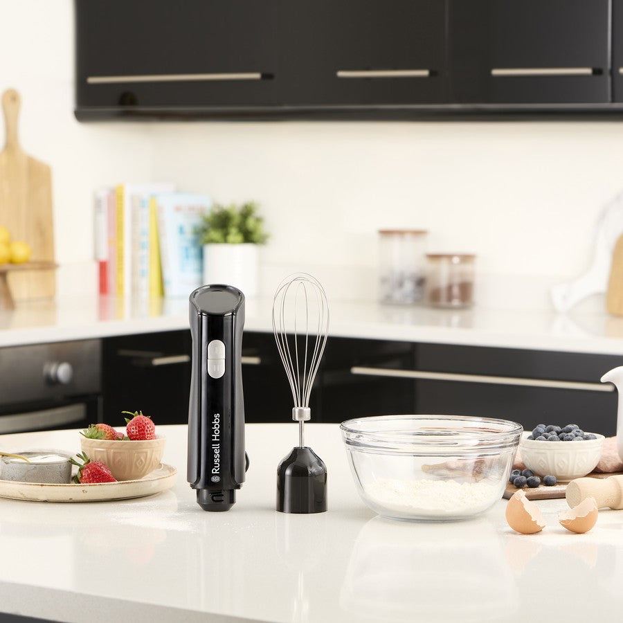 Black handheld mixer on a kitchen counter with a bowl and ingredients.