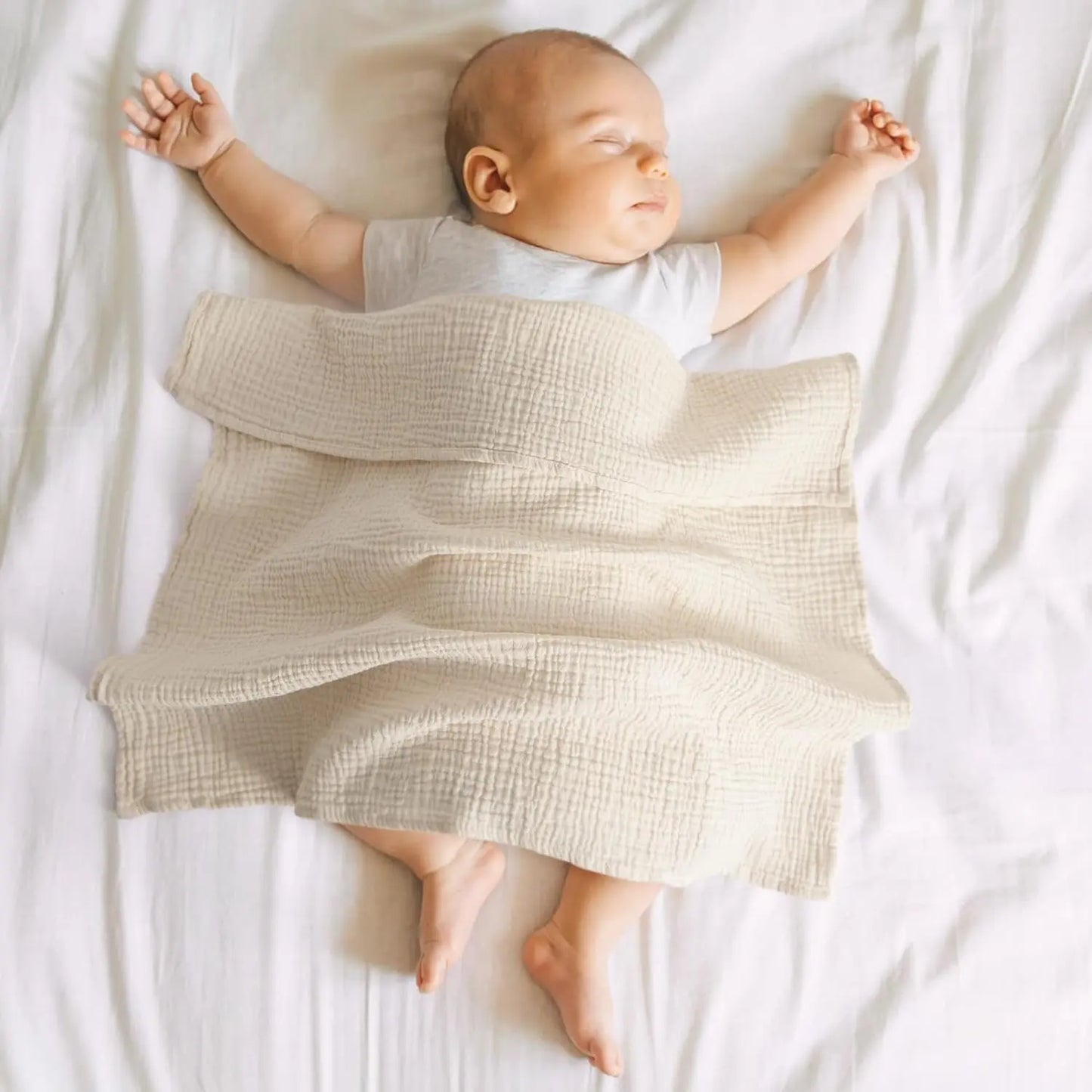 Baby lying on a white blanket with a textured beige blanket draped over them