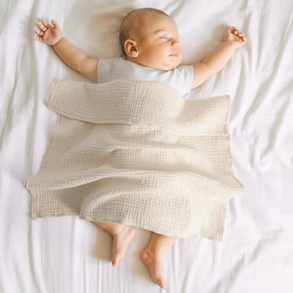 Baby lying on a white blanket with a textured beige blanket draped over them