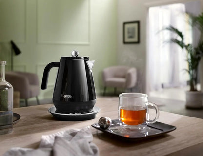 Black electric kettle on a wooden table with a cup of tea in a cozy room.