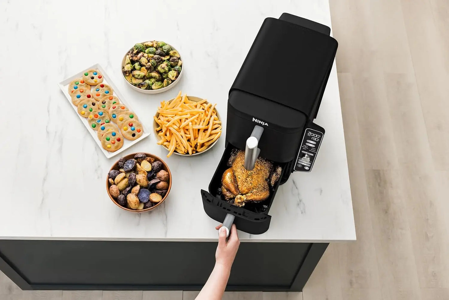 Black air fryer on a kitchen counter with various food items around