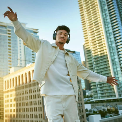 Man in a beige jacket and pants standing in an urban setting with tall buildings.