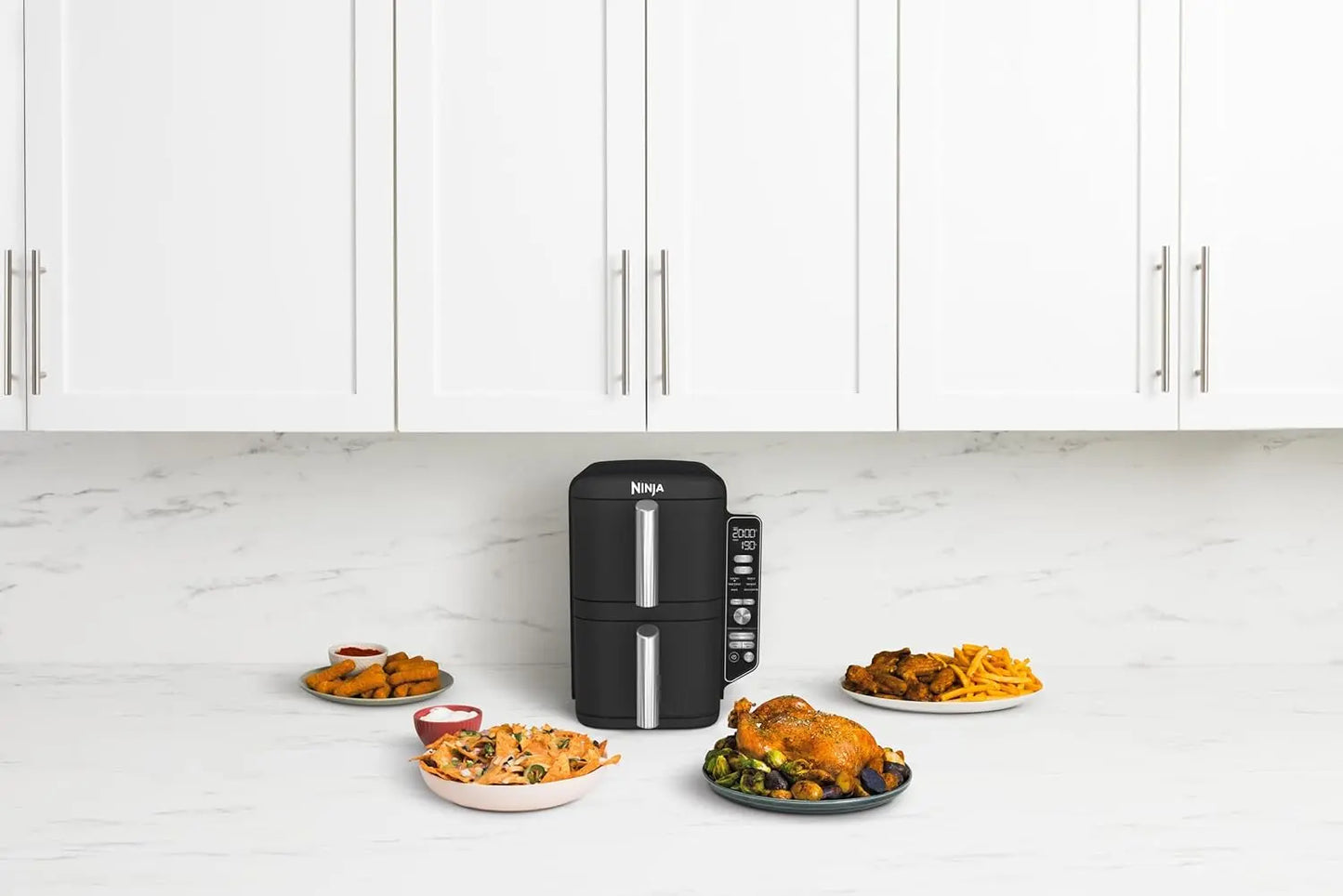 Black air fryer on a kitchen counter with plates of food