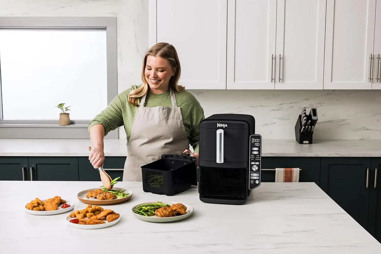 Woman in a kitchen using a Ninja foodi multicooker with plates of food on the counter.
