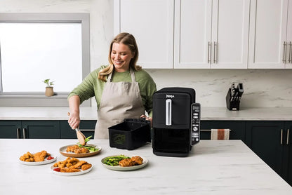 Woman in a kitchen using a Ninja foodi multicooker with plates of food on the counter.