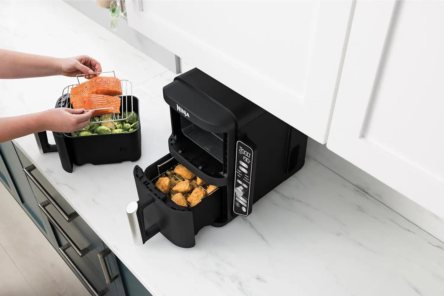 Black countertop air fryer with food being added on a white kitchen counter.