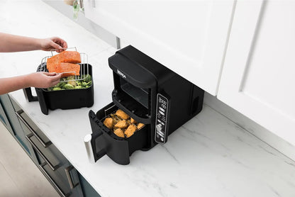Black countertop air fryer with food being added on a white kitchen counter.