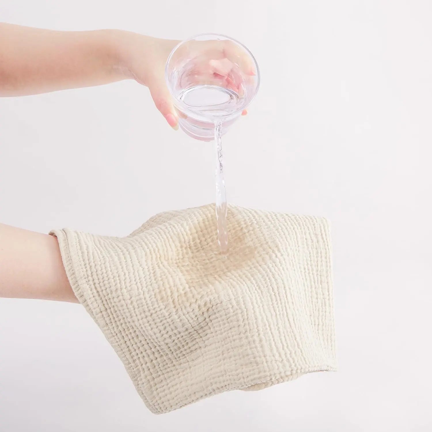Person pouring water from a glass into a beige towel on a white background