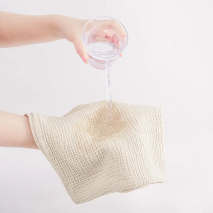 Person pouring water from a glass into a beige towel on a white background