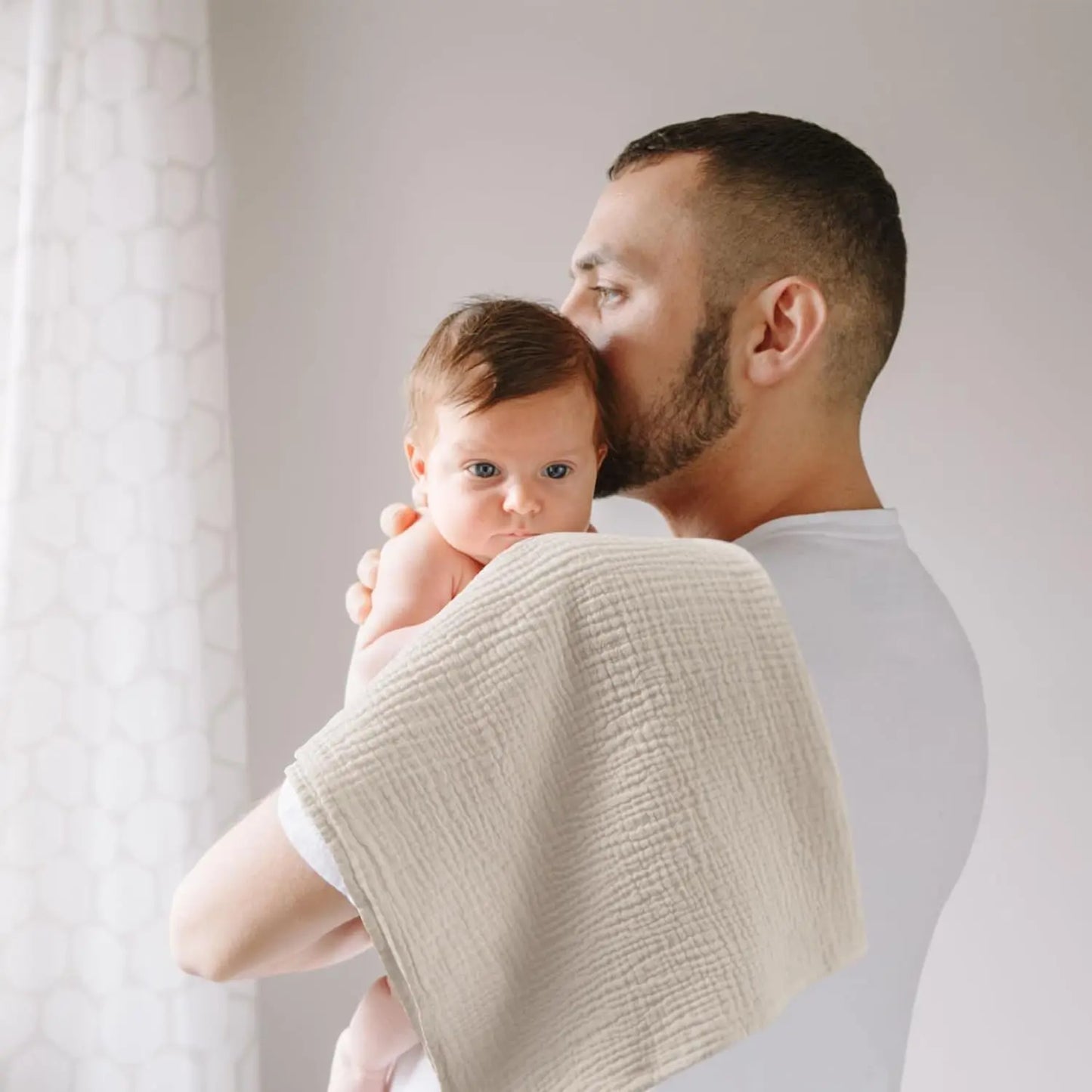 Man holding a baby wrapped in a beige blanket against a light background