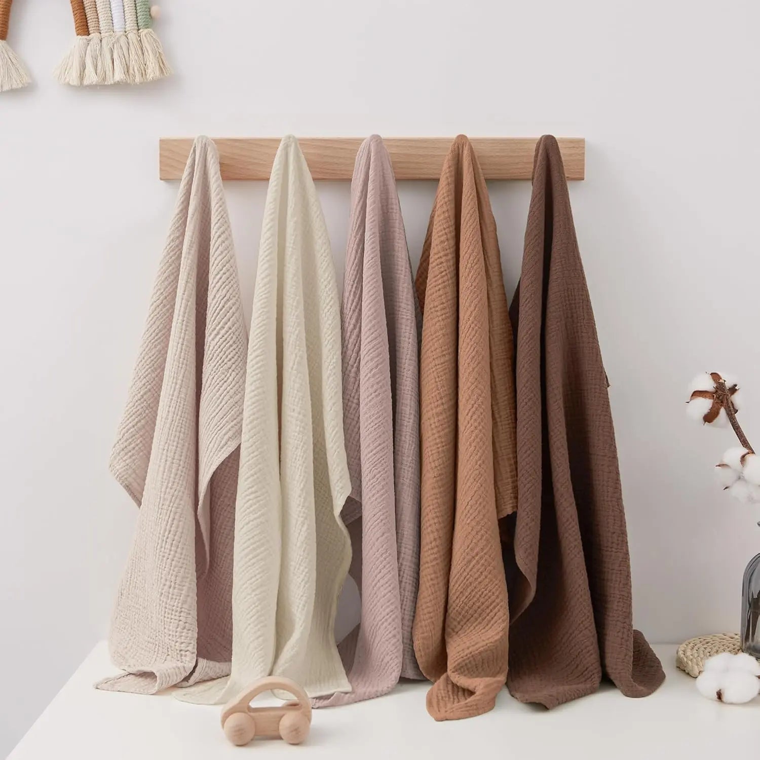 Set of five knitted blankets in various colors hanging on a wooden rod against a white wall.