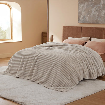 Neatly made bed with a textured beige blanket in a softly lit bedroom.