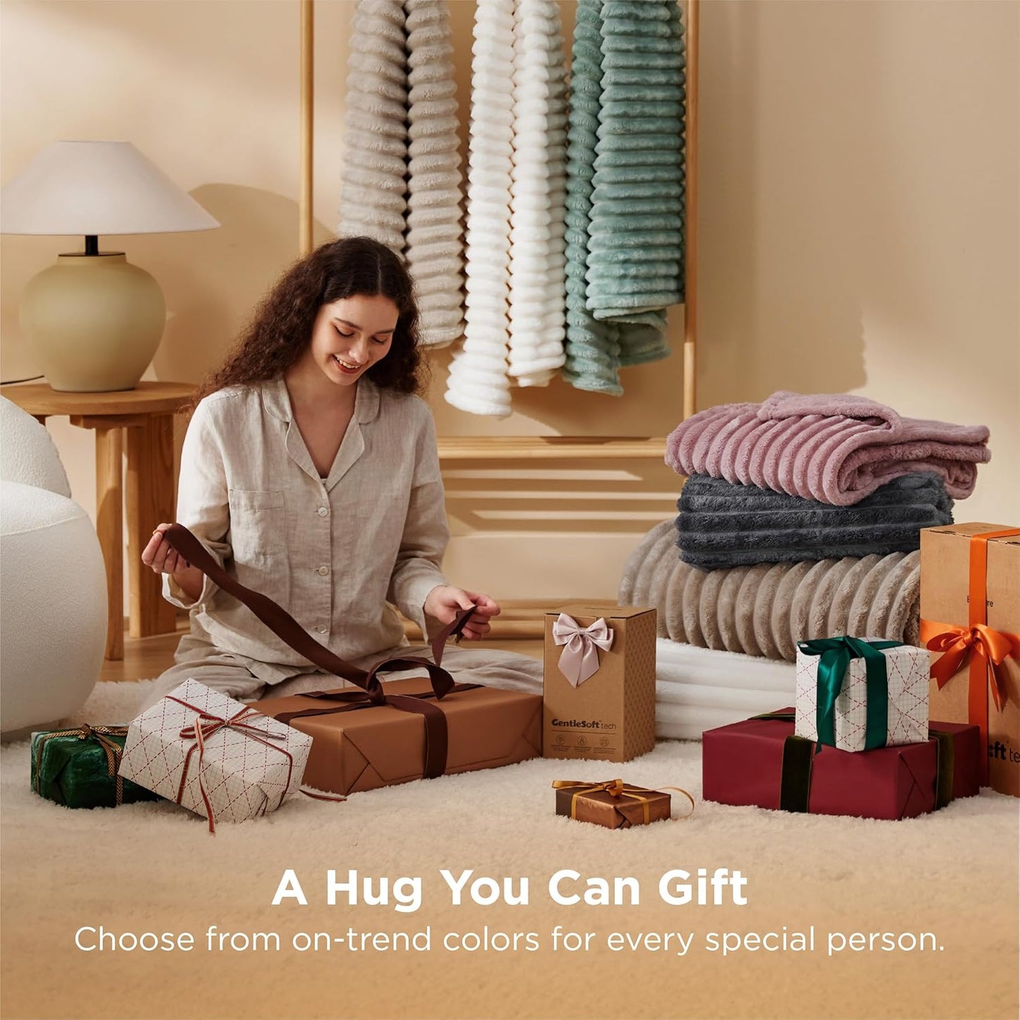 Woman wrapping gifts in a cozy room with folded blankets and a lamp.
