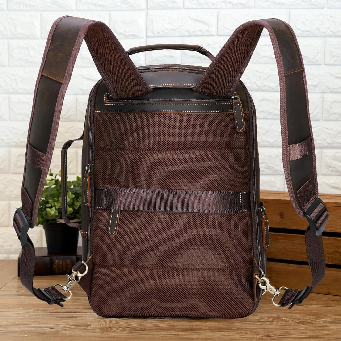 Brown backpack with leather straps on a wooden surface with a white brick wall background