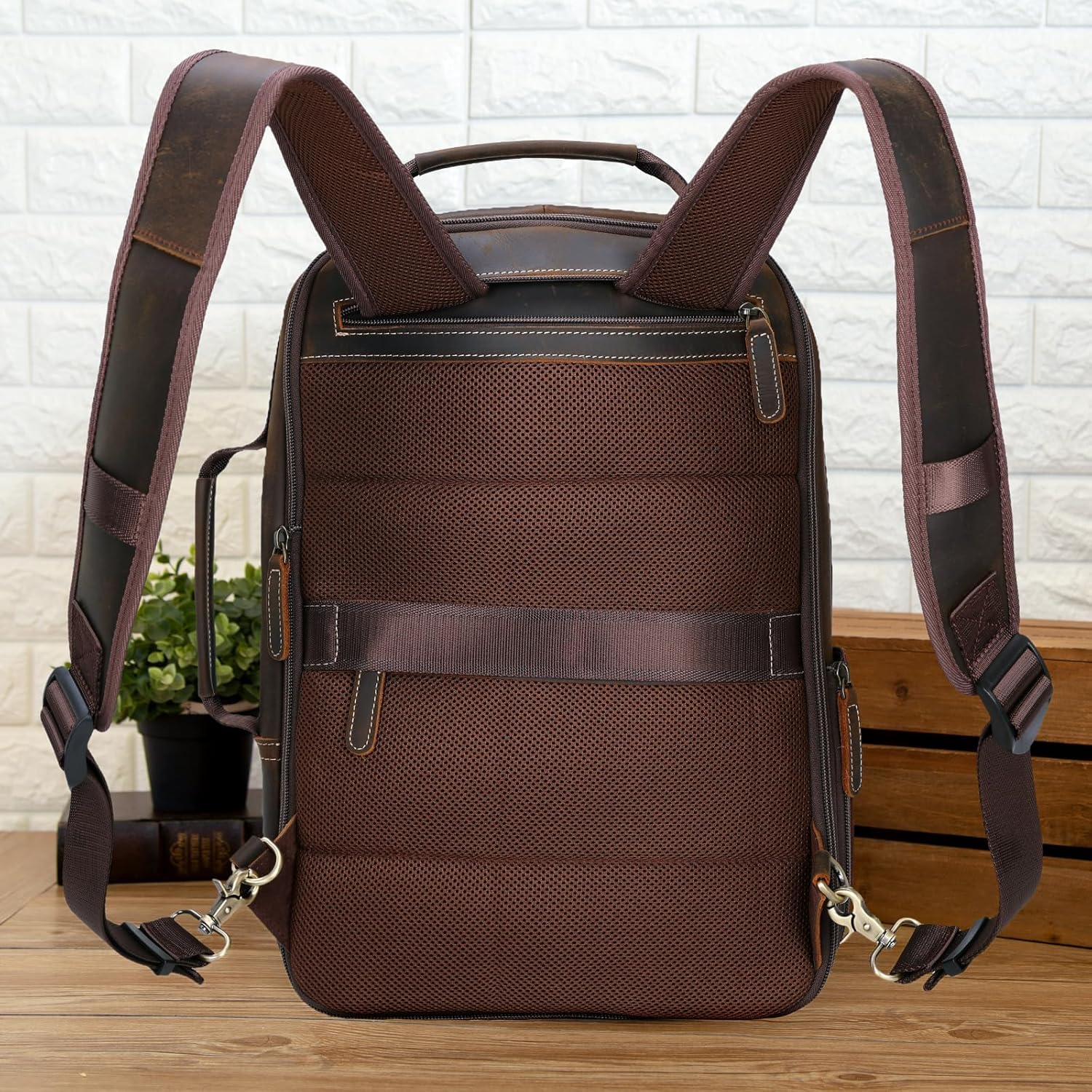 Brown backpack with leather straps on a wooden surface with a white brick wall background