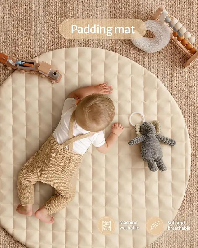 Baby playing on a round padding mat with toys on a textured beige floor.