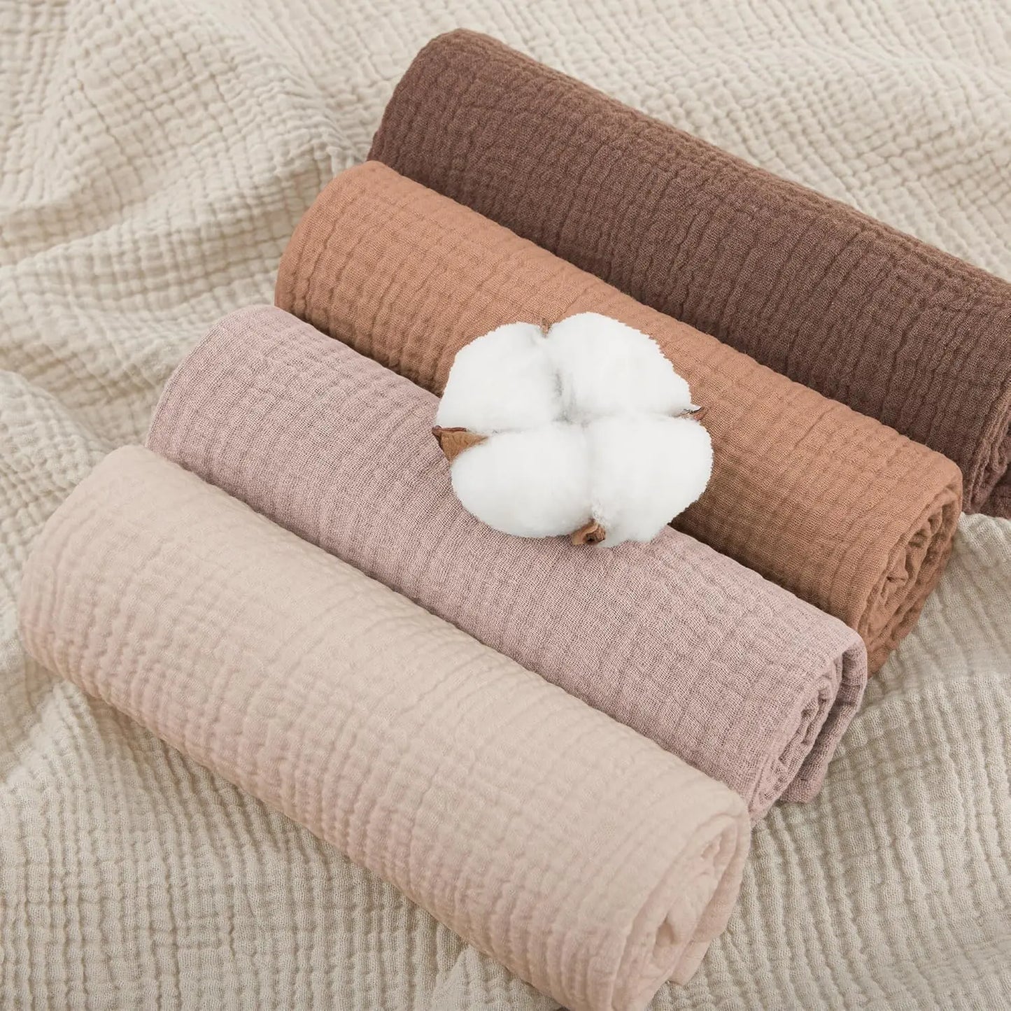 Four rolled-up fabrics in brown, pink, and beige with a cotton ball on a textured beige background.
