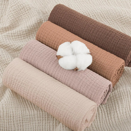 Four rolled-up fabrics in brown, pink, and beige with a cotton ball on a textured beige background.