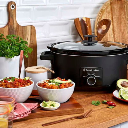Crockpot on a kitchen counter with bowls of food and kitchen utensils.