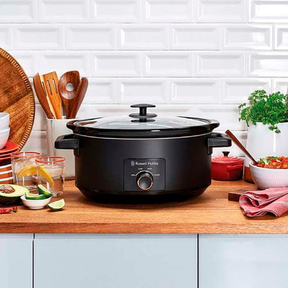 Black slow cooker on a kitchen counter with utensils and ingredients.