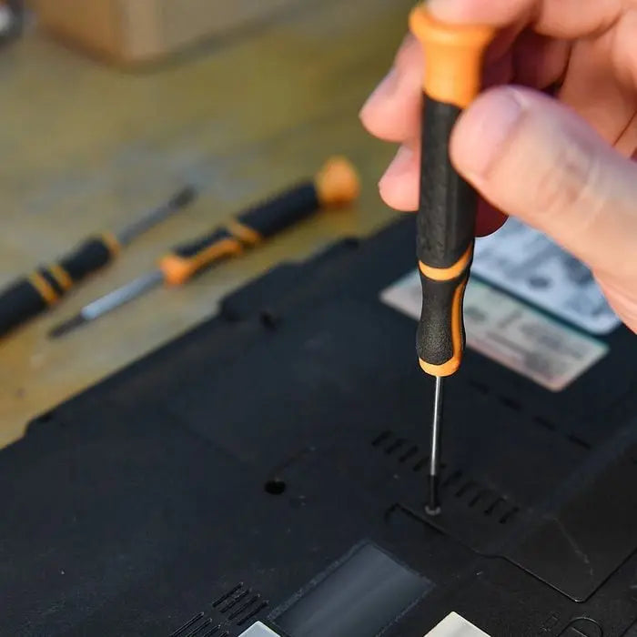 Hand using a screwdriver to work on a laptop with other tools in the background.