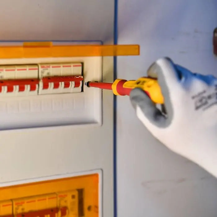 Hand using a screwdriver to adjust components inside an electrical panel.