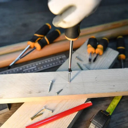 Person using a screwdriver on a wooden surface with tools and screws around
