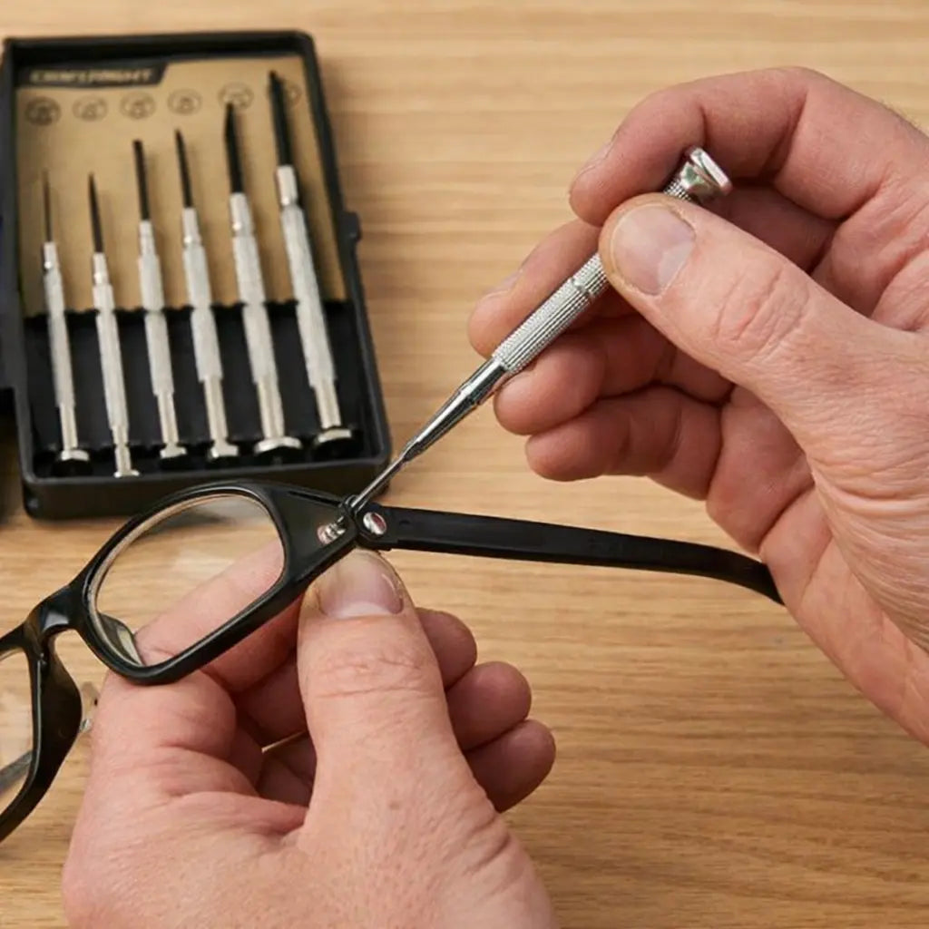 Person adjusting eyeglasses with a tool, set against a wooden surface.