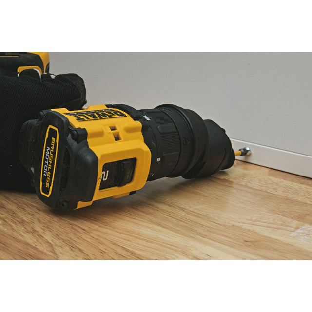 A DeWalt cordless drill driver with a black and yellow body, resting on a light wood floor against a white baseboard.