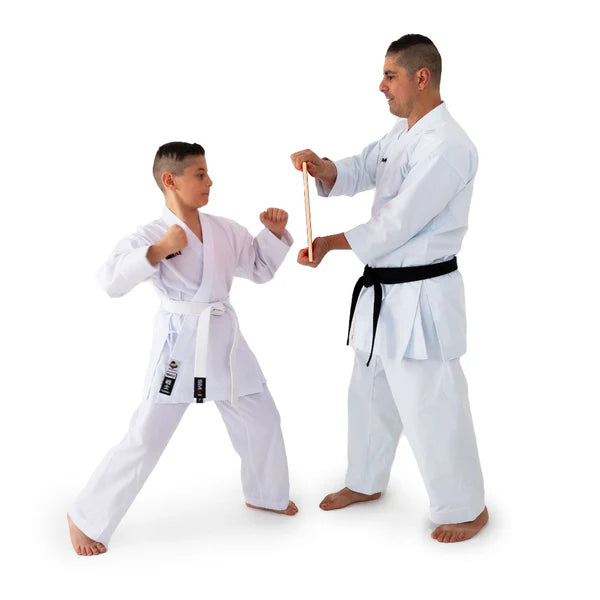 An adult and a child wearing white martial arts uniforms with belts, practicing a wooden stick strike on a plain white background.