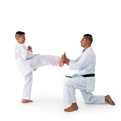 A man and a young boy in white martial arts uniforms practice a kick in a studio setting against a plain white background.