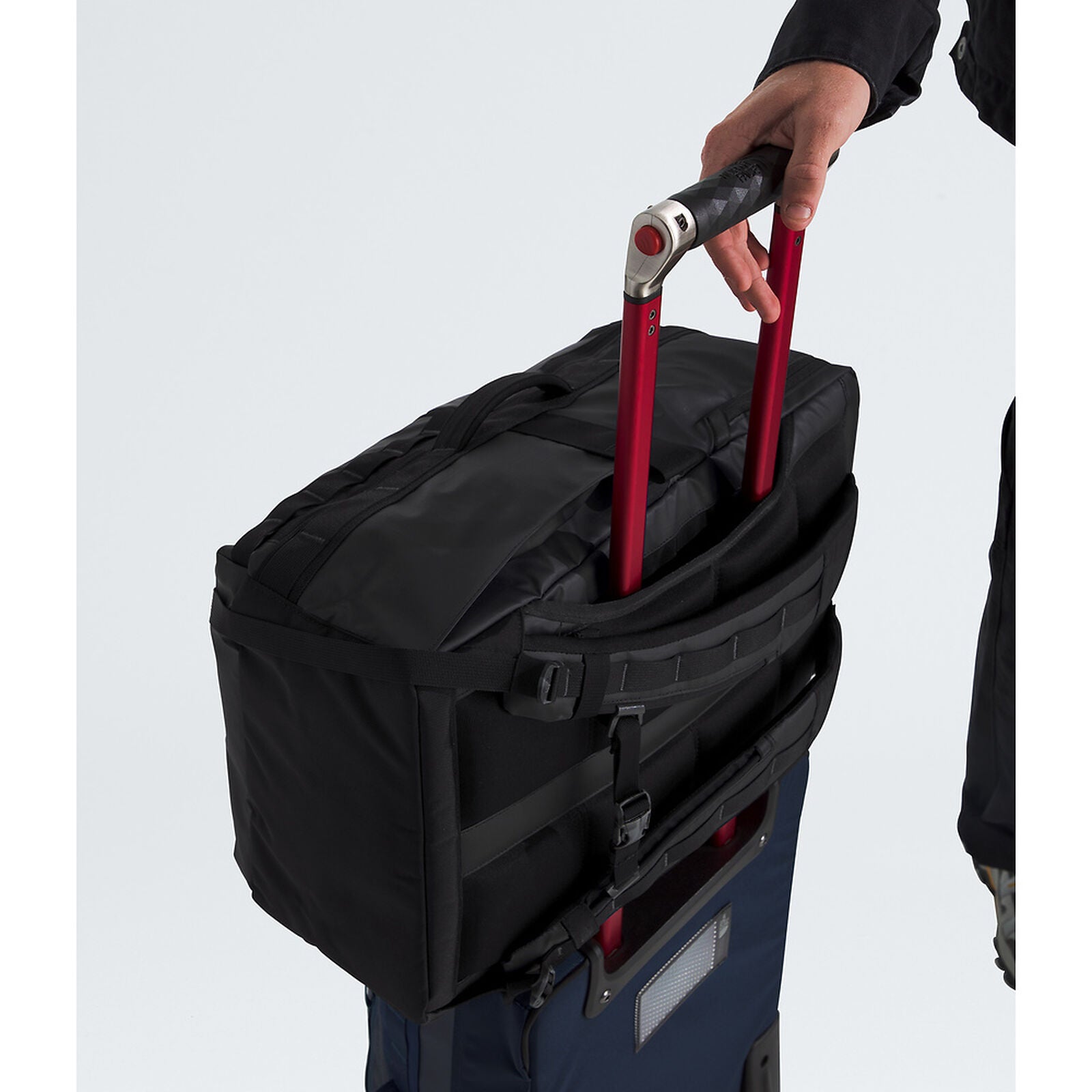 Person pulling a black suitcase with red handle on a light gray background