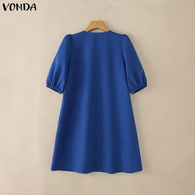 Blue dress on a hanger against a beige background with 'VONDA' branding.