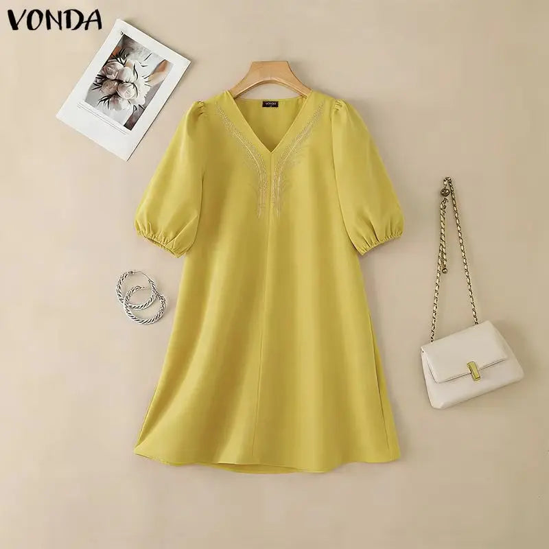 Yellow dress on a hanger with a white handbag and necklace on a beige background, featuring the brand 'Vonda'.