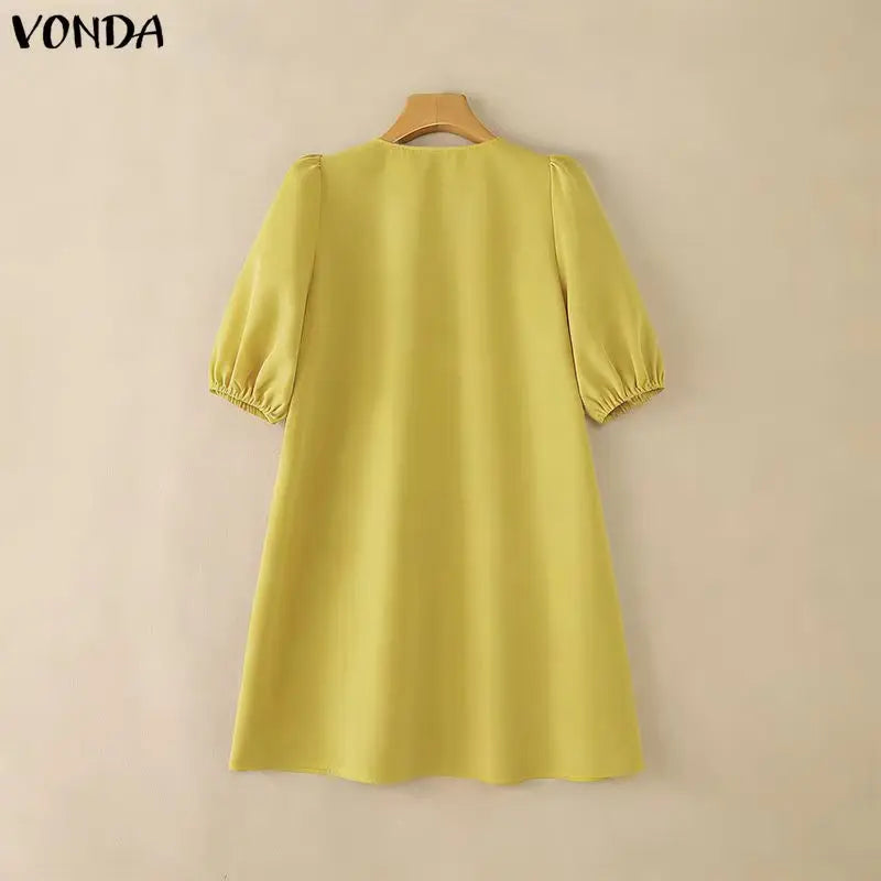 Yellow dress on a hanger against a beige background with 'Vonda' branding.