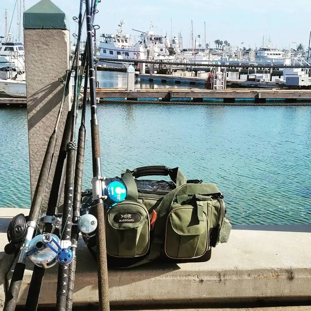 Fishing rods and green tackle bag on a dock with water and boats in the background