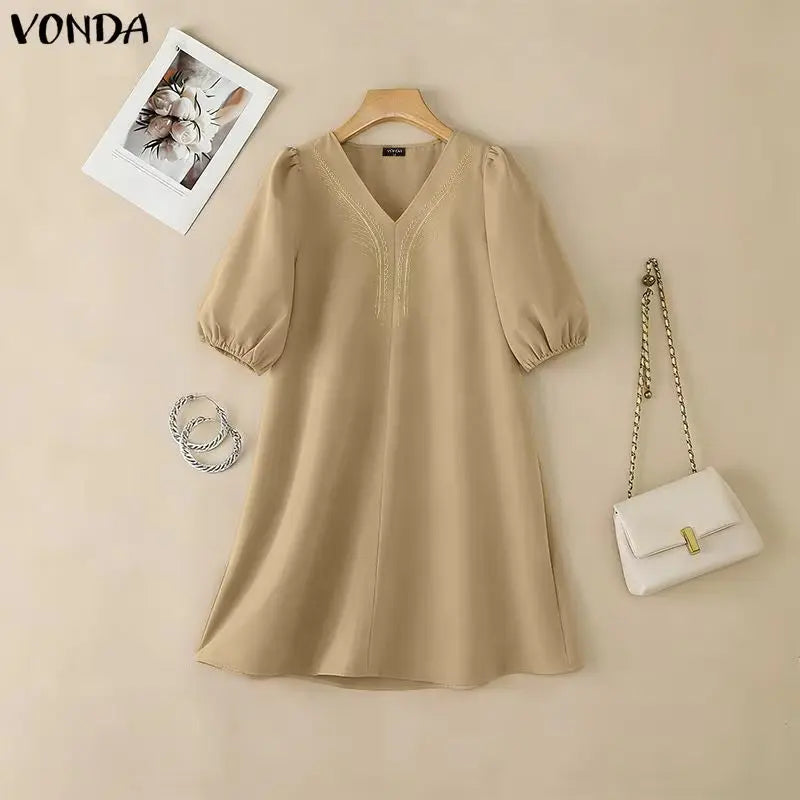 Beige dress on a hanger with a white handbag and necklace on a beige background, featuring the brand 'Vonda'.