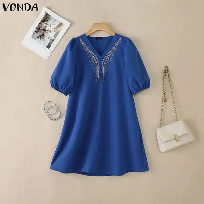 Blue dress with embroidery on a beige background, accompanied by a white handbag and photo frame.