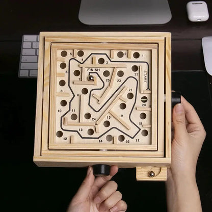 Wooden maze game held by a hand with a computer keyboard in the background
